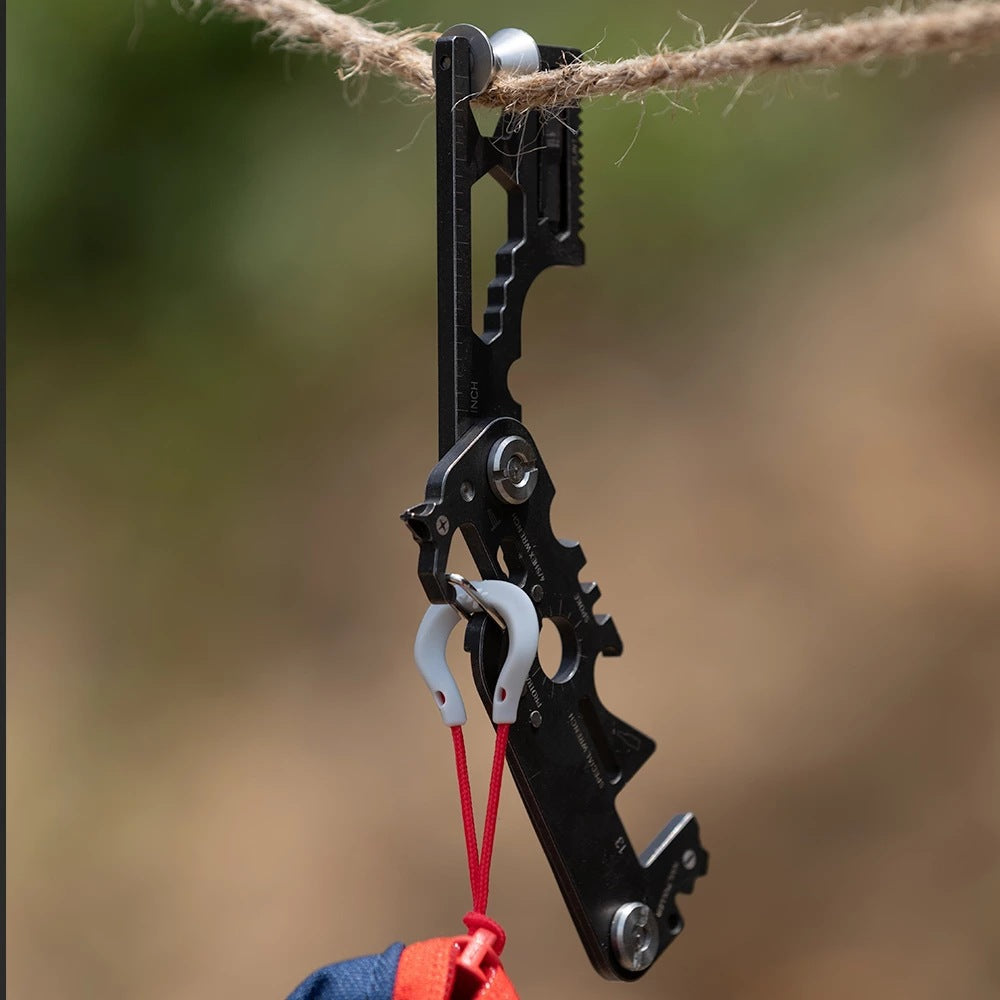Multitool hanging from a rope outdoors showing carabiner clip and blade